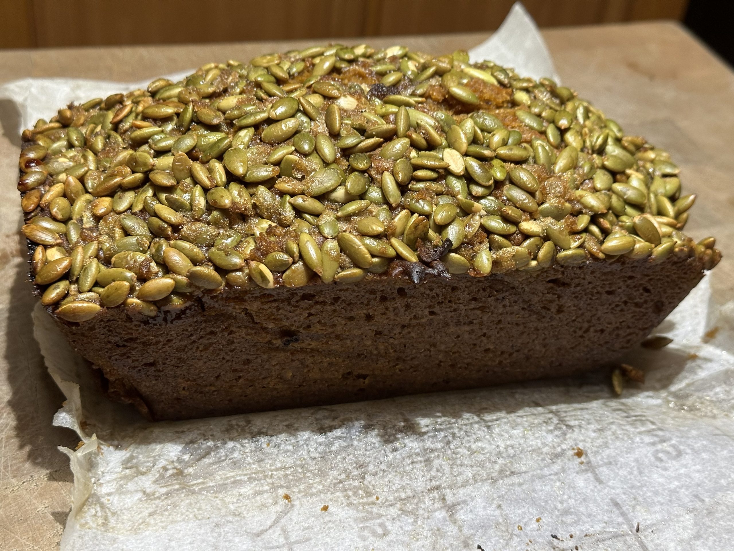 A loaf of cooked pumpkin bread with pepitas on top.